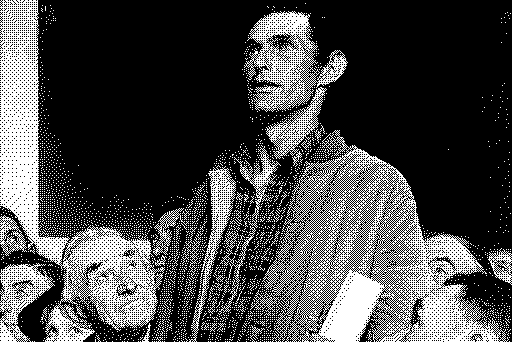 A black-and-white image of a man standing in the center, looking upward, surrounded by a crowd of people with varied expressions.
